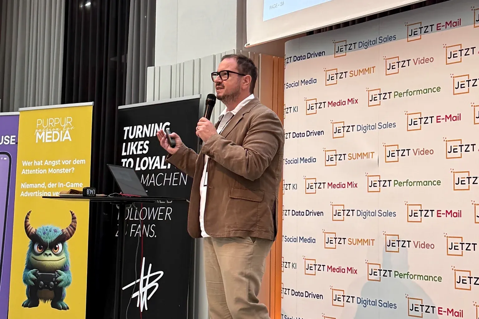 Armin Rogl on stage during a keynote, gesturing towards the screen